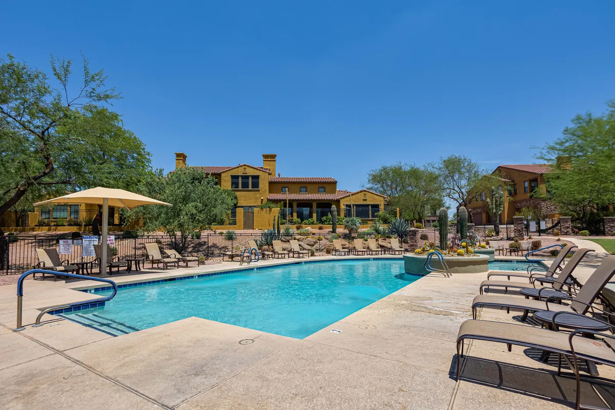 A cheerful exterior scene with a swimming pool, lounge chairs, landscaped gardens, and a yellow building in the background. The area looks lively and welcoming, suggesting opportunities for social gatherings, sunbathing, and relaxation under the sun.