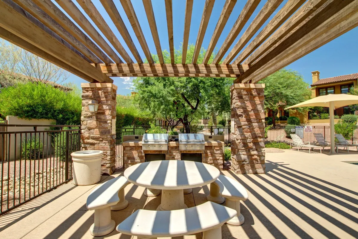 A stylish outdoor dining area featuring a large table, grill, pergola, and lush greenery. The setting is casual and inviting, ideal for hosting barbecues, family meals, or social gatherings. The space is private yet open, suggesting exclusivity and comfort.