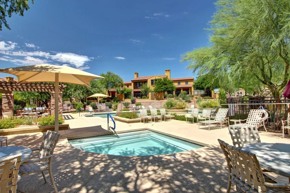 A beautifully landscaped swimming pool area complete with outdoor seating and a pergola, surrounded by lush gardens. The scene suggests opportunities for relaxation, sunbathing, social gatherings, and enjoying Scottsdale's warm weather.
