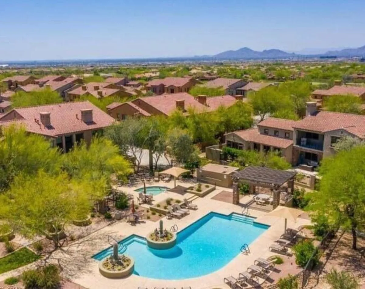 An inviting exterior pool area surrounded by landscaped gardens and nearby homes. The sparkling swimming pool, ample lounging spaces, and community backdrop create a relaxed, resort-style atmosphere.