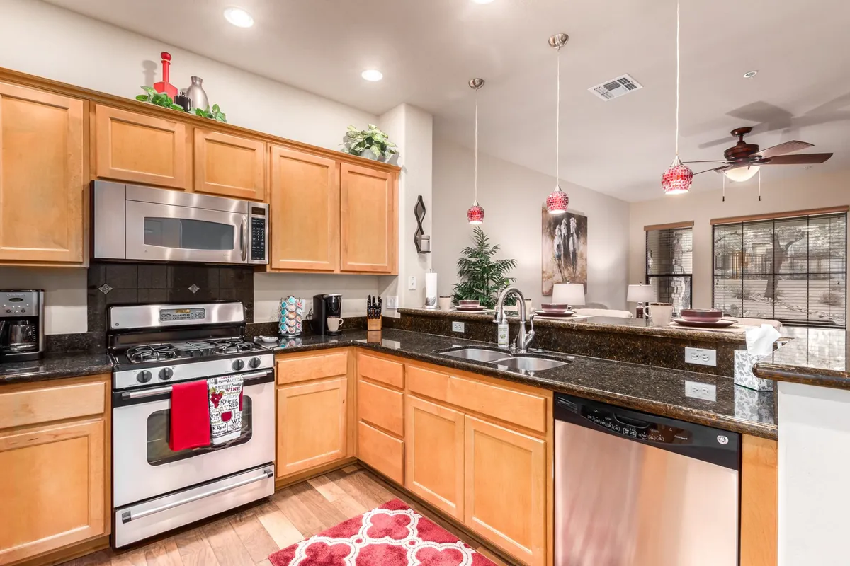 This image showcases a spacious kitchen with a granite countertop, stainless steel appliances, and inviting red pendant lights. The scene hints at meal preparation, gatherings, and a warm, welcoming atmosphere.