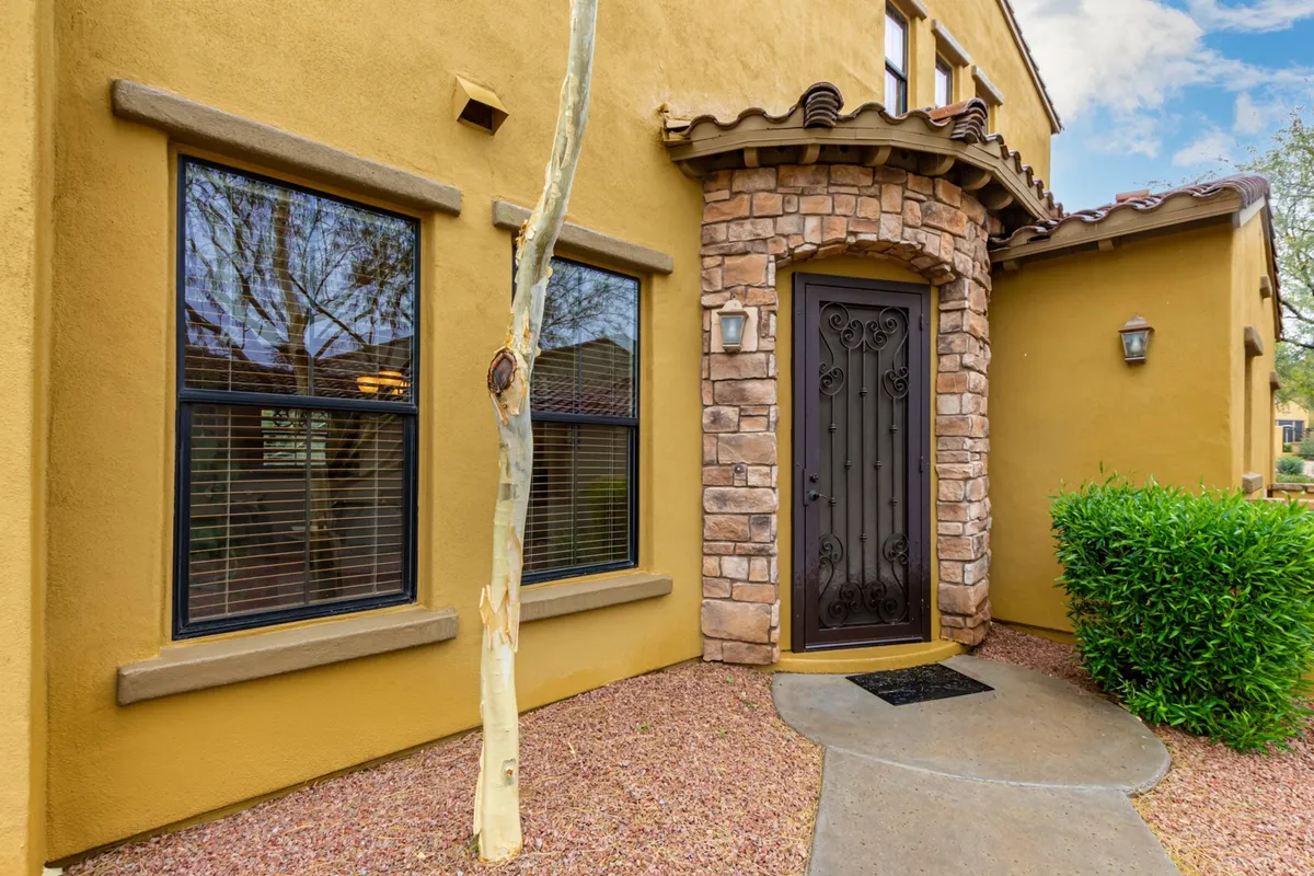 A welcoming exterior view of the townhome, featuring a decorative front door, a charming stone archway, and manicured landscaping. The entrance exudes an inviting and secure feel, giving guests a first impression of comfort and convenience.