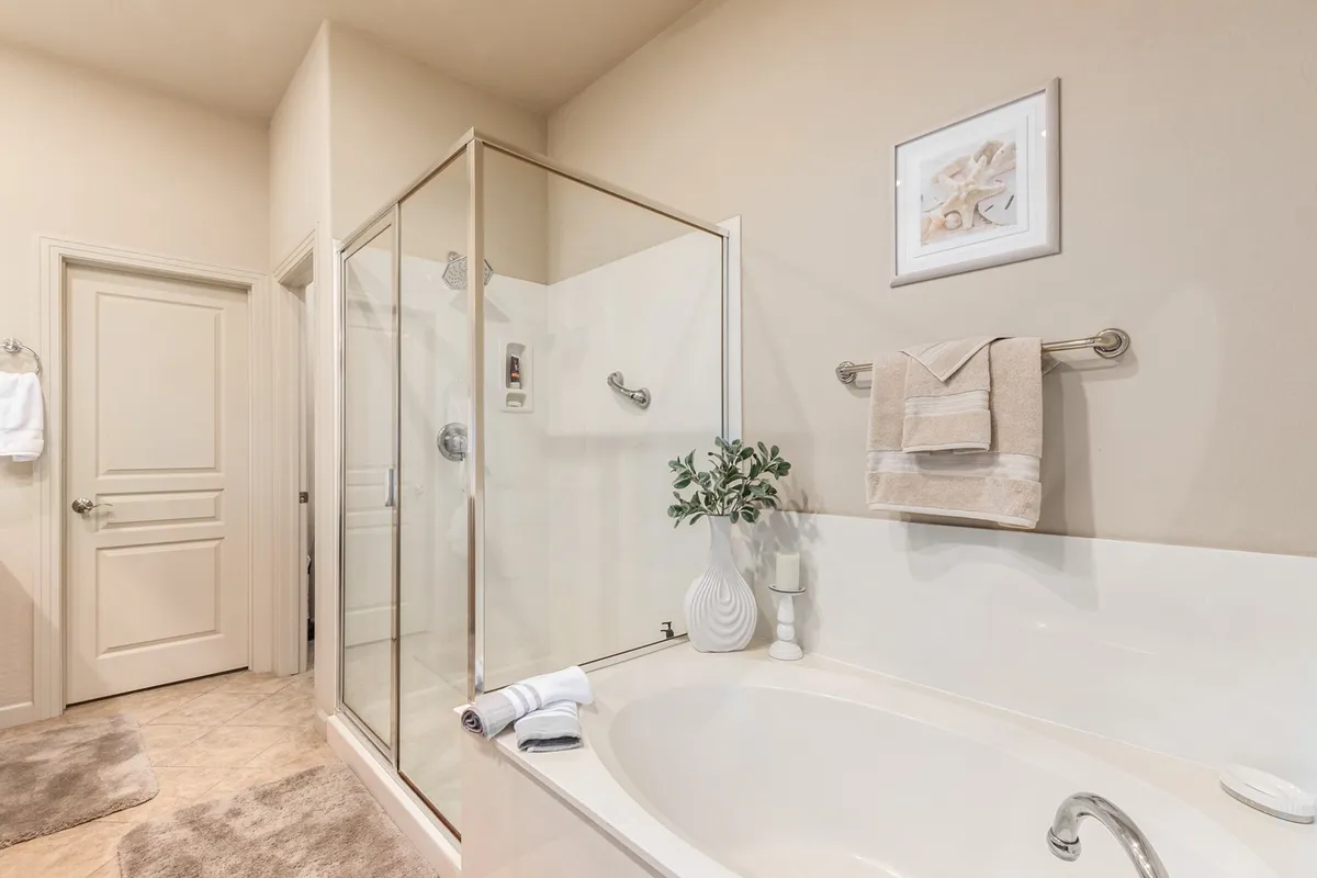 A bright and inviting bathroom featuring a modern bathtub, a glass-enclosed walk-in shower, fresh towels, and a decorative plant. The space exudes a spa-like feel, ideal for relaxation and self-care.