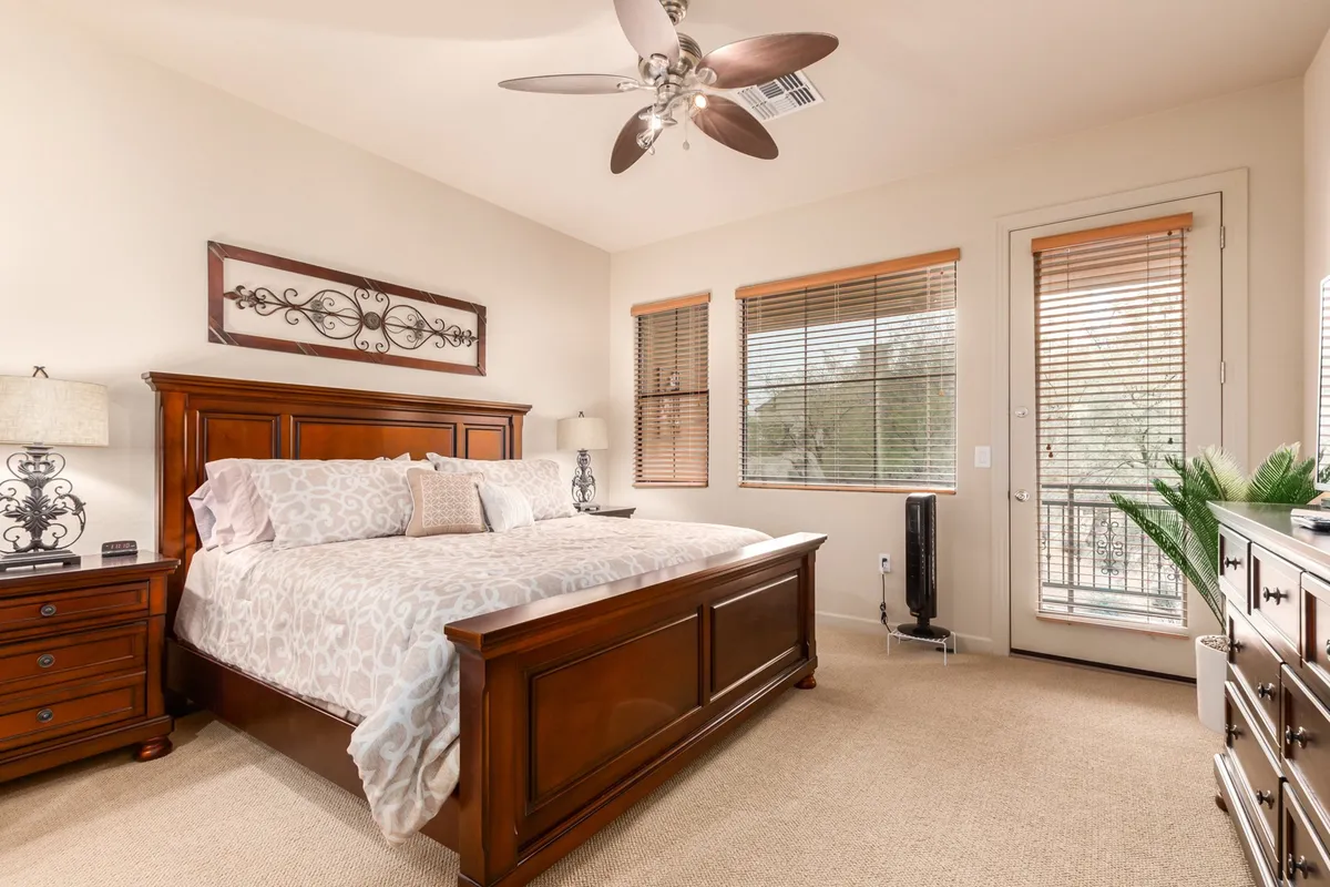 A serene bedroom with a comfortable bed, a large window allowing natural light to fill the space, a dresser, and a side table with a lamp. The tranquil atmosphere suggests a restful retreat, and the room appears spacious and uncluttered.