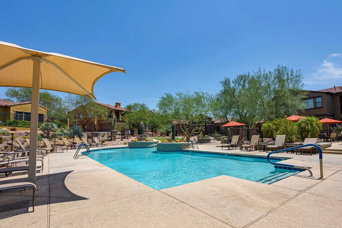 A sparkling swimming pool surrounded by lounge chairs, umbrellas, and lush landscaping. The pool area appears inviting and perfect for families, with ample seating and space for relaxation and socializing. The setting is enhanced by well-maintained greenery and open sky, evoking a resort-like atmosphere.